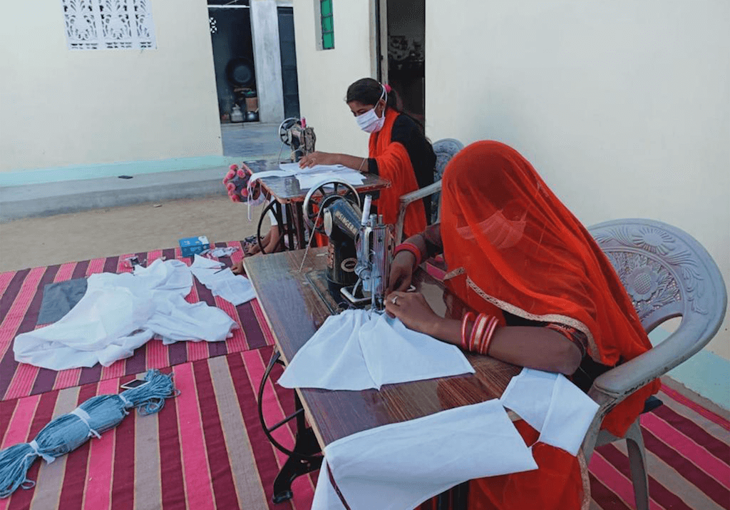 Artisans sewing white fabric in a courtyard.