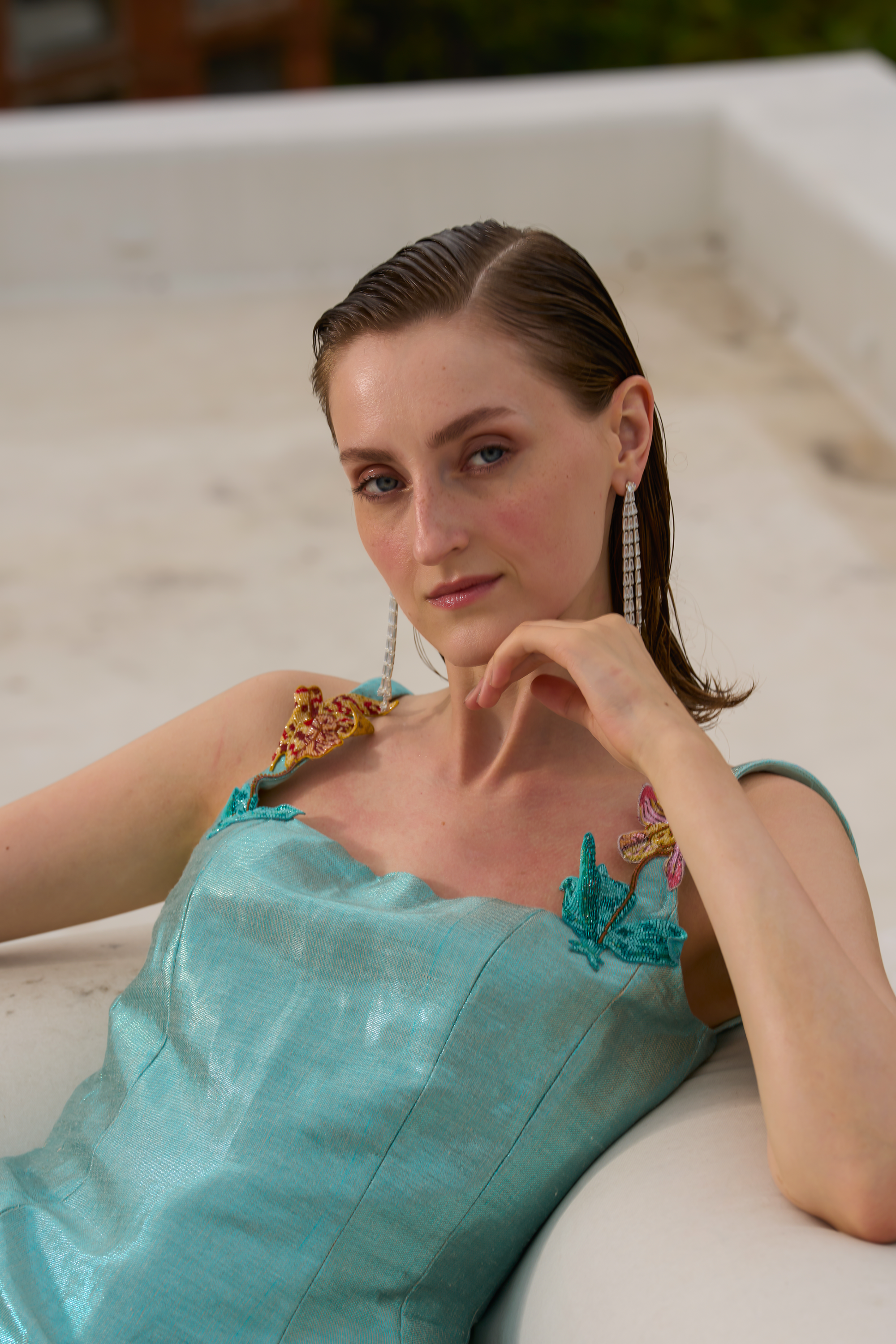 Woman in a turquoise dress with floral details sitting on a white surface.