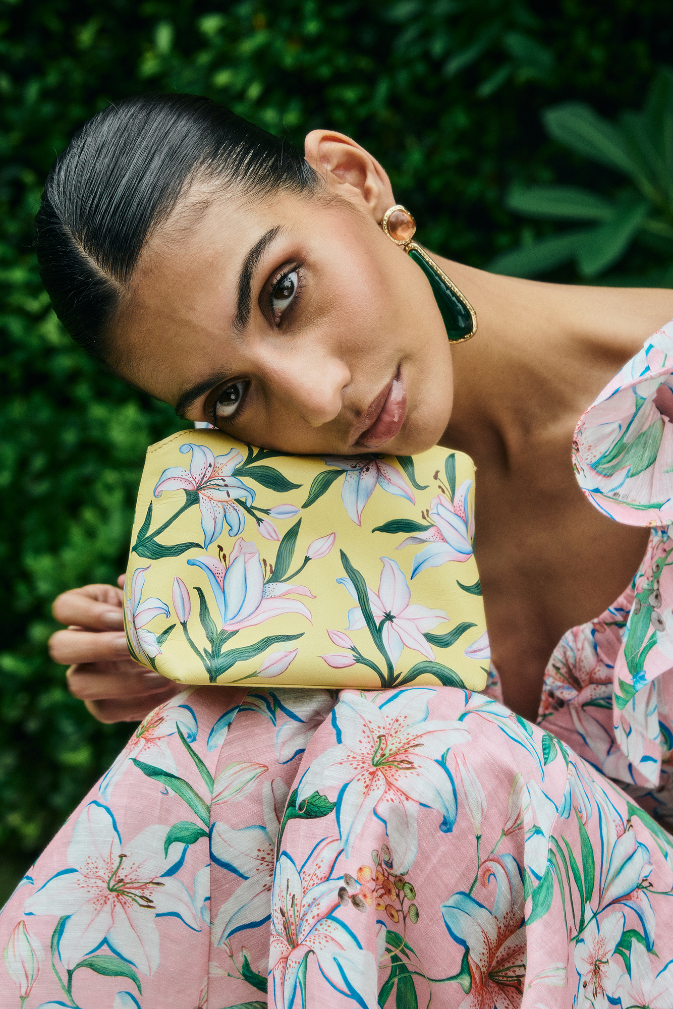 Woman holding a floral clutch against a green leafy background
