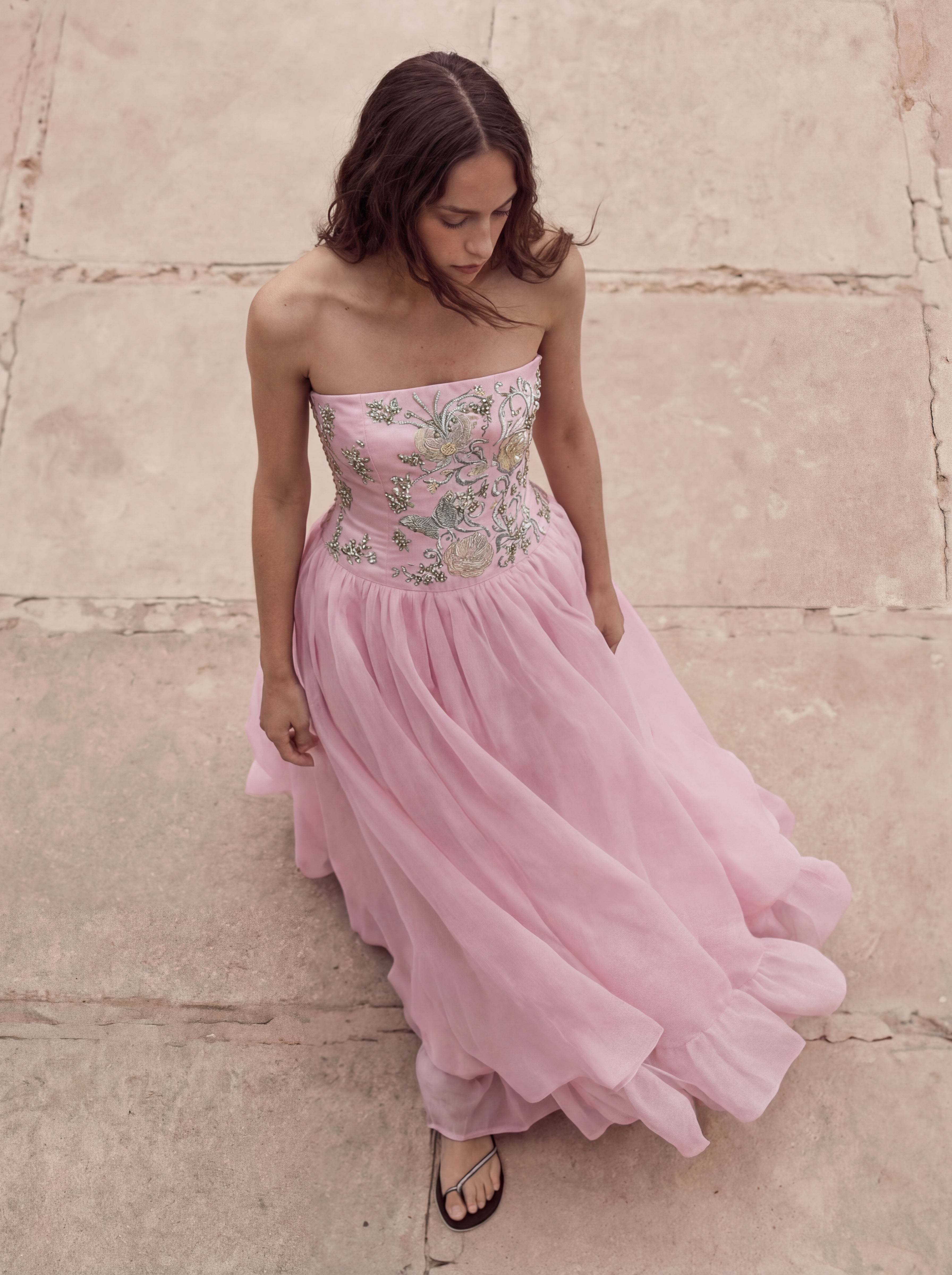 Woman wearing a pink strapless dress with floral embroidery on a stone pavement.
