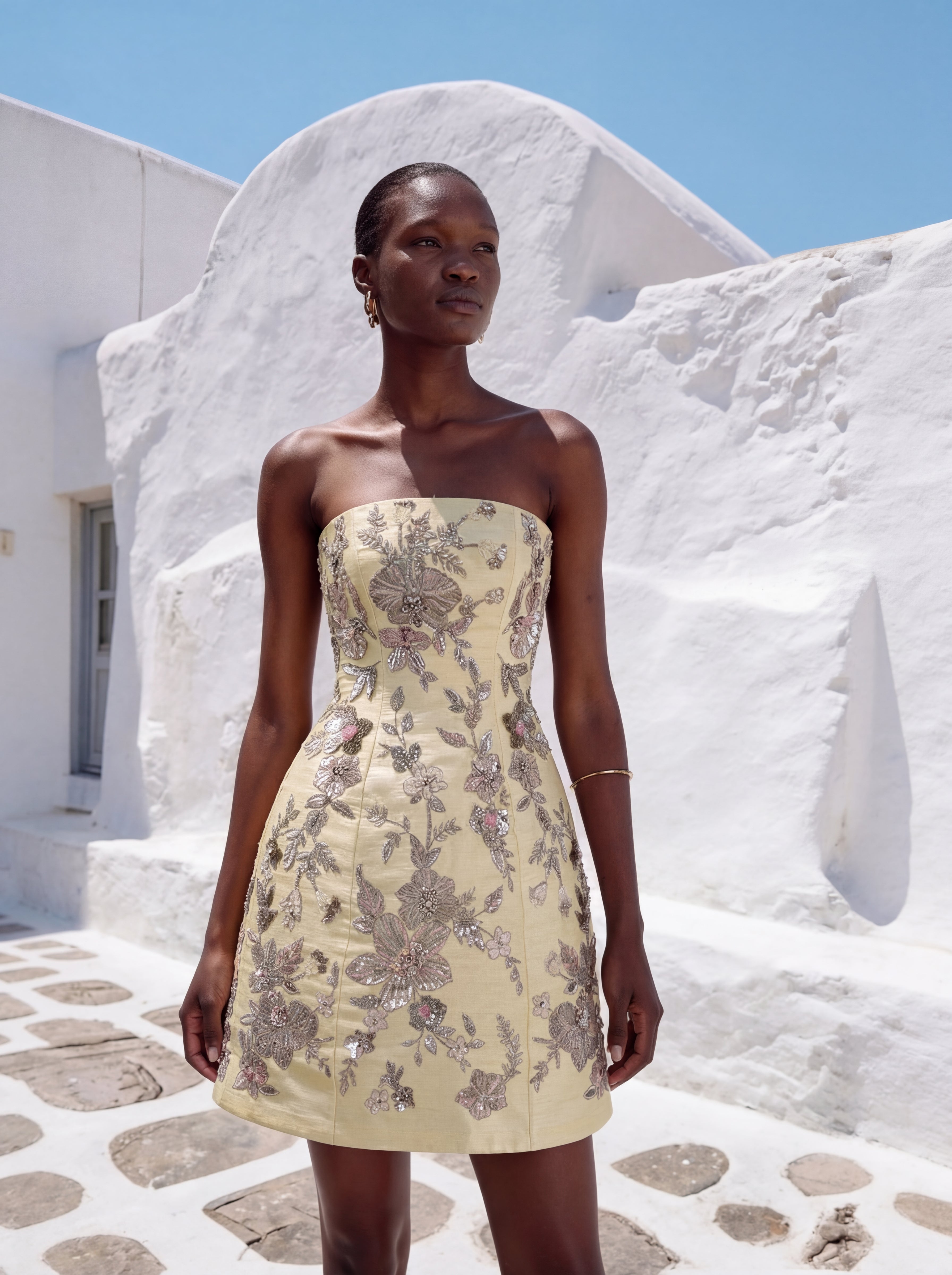 Woman wearing a strapless floral dress in front of white Cycladic architecture.