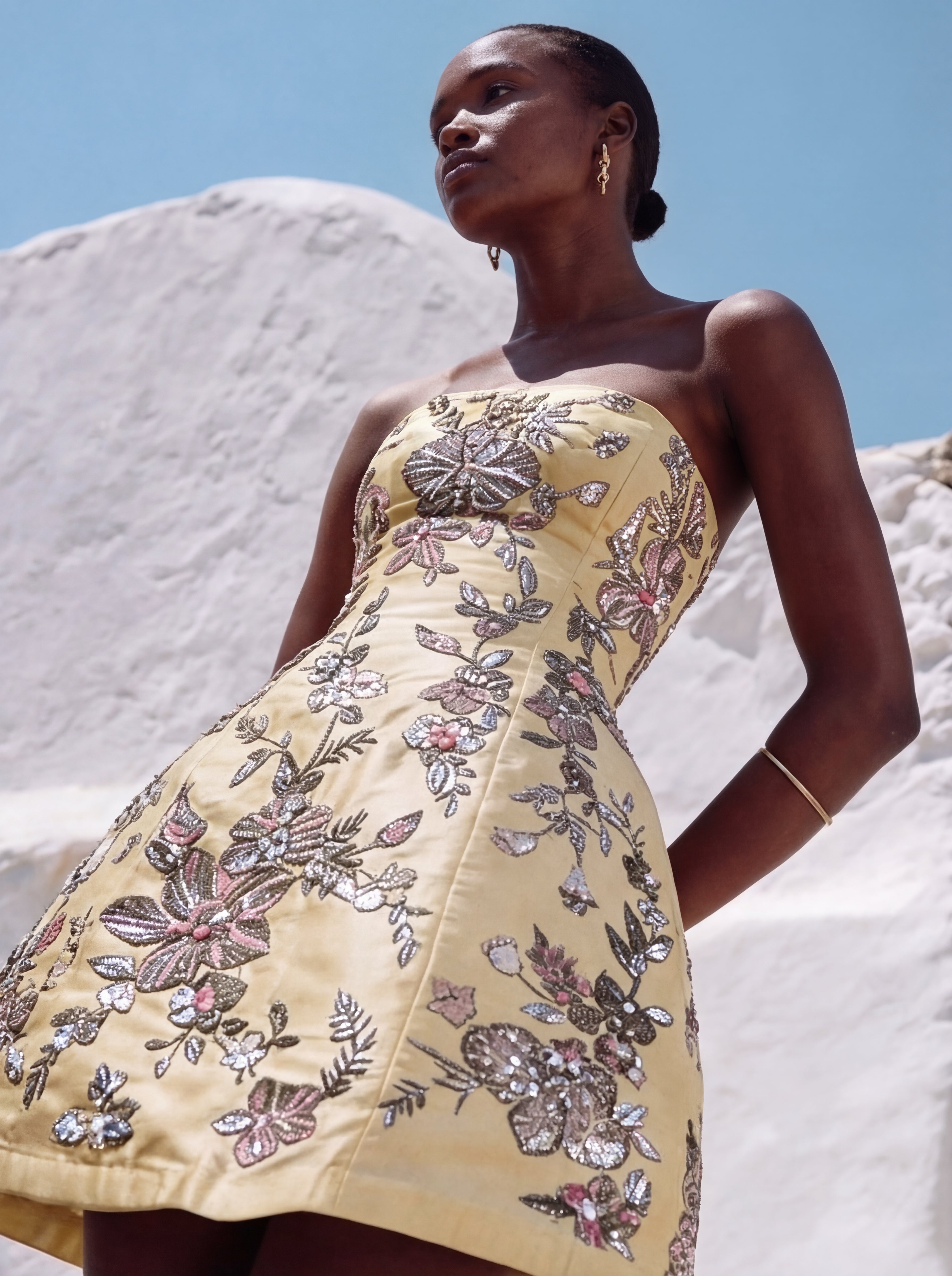 Woman wearing a yellow floral dress against a white sand and blue sky background