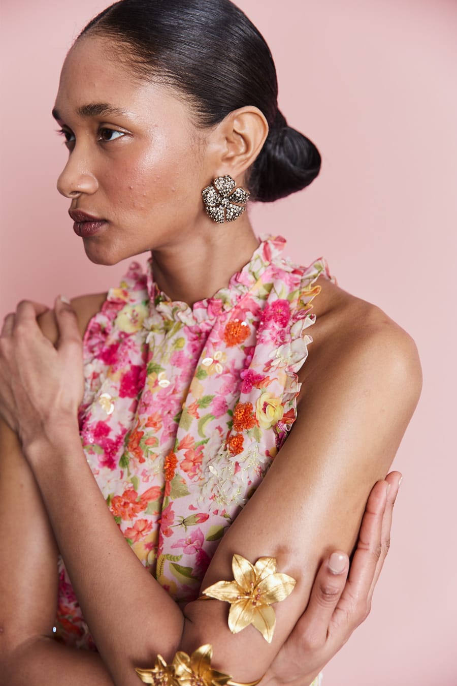 Woman wearing a floral scarf and gold arm bands against a pink background