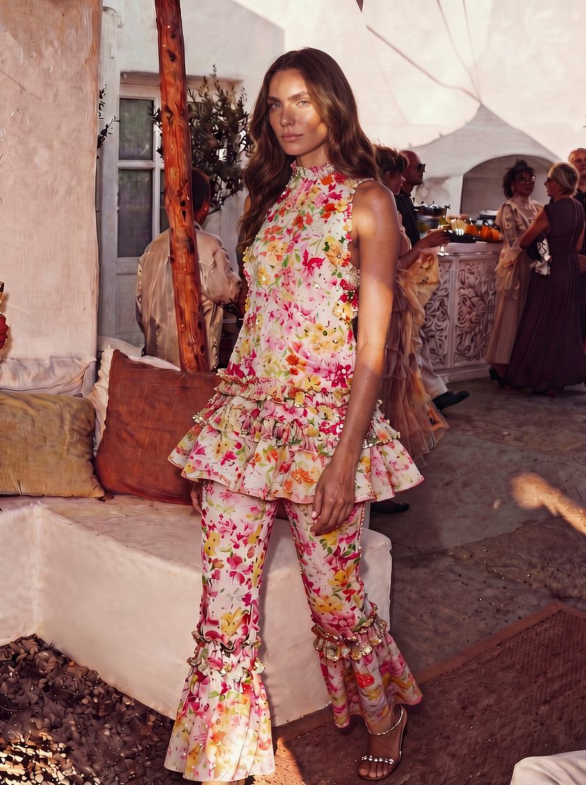 Woman in a floral dress and pants sitting on a white bench outdoors.