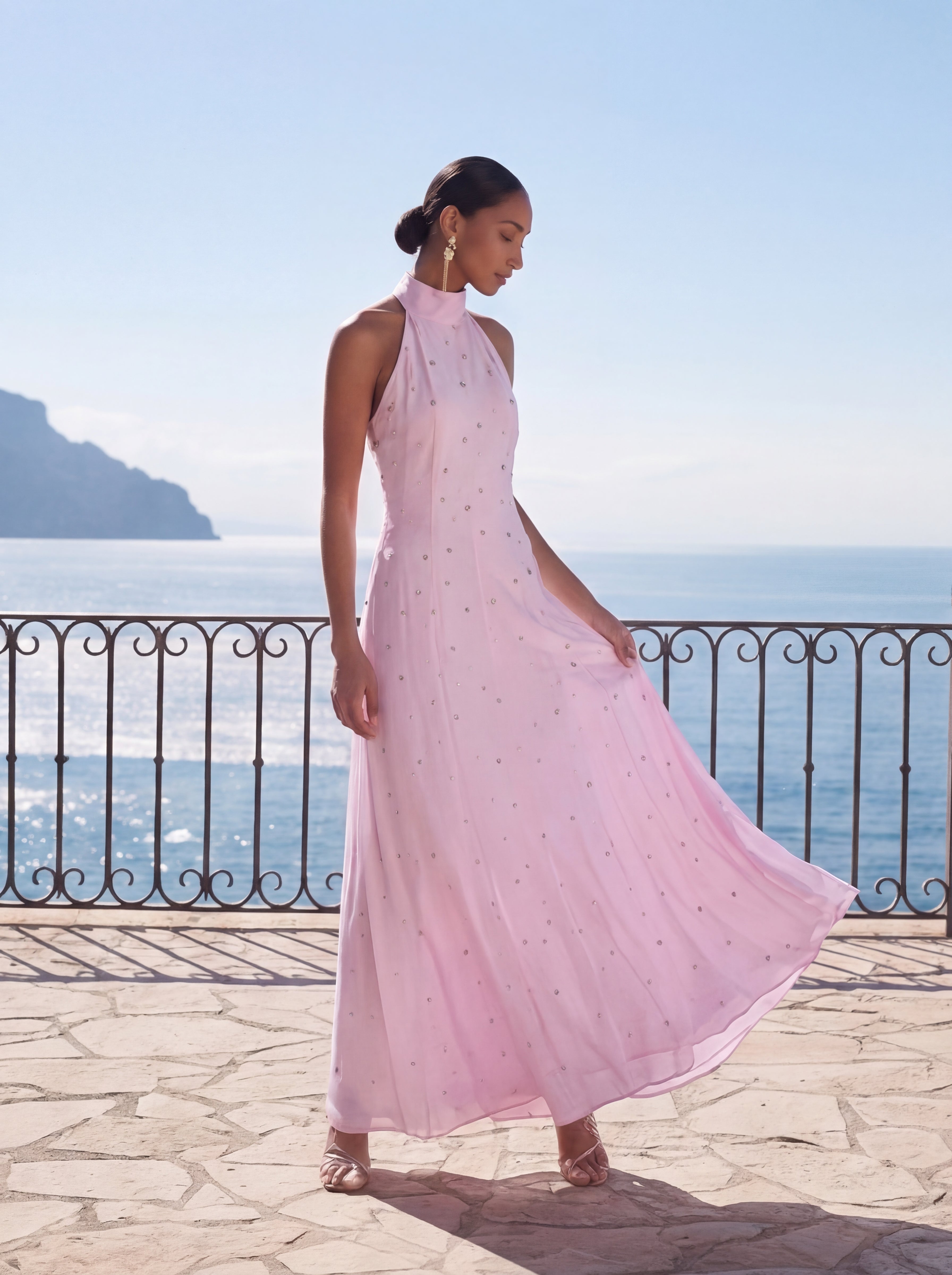 Woman in a pink dress standing on a balcony with a scenic ocean view.
