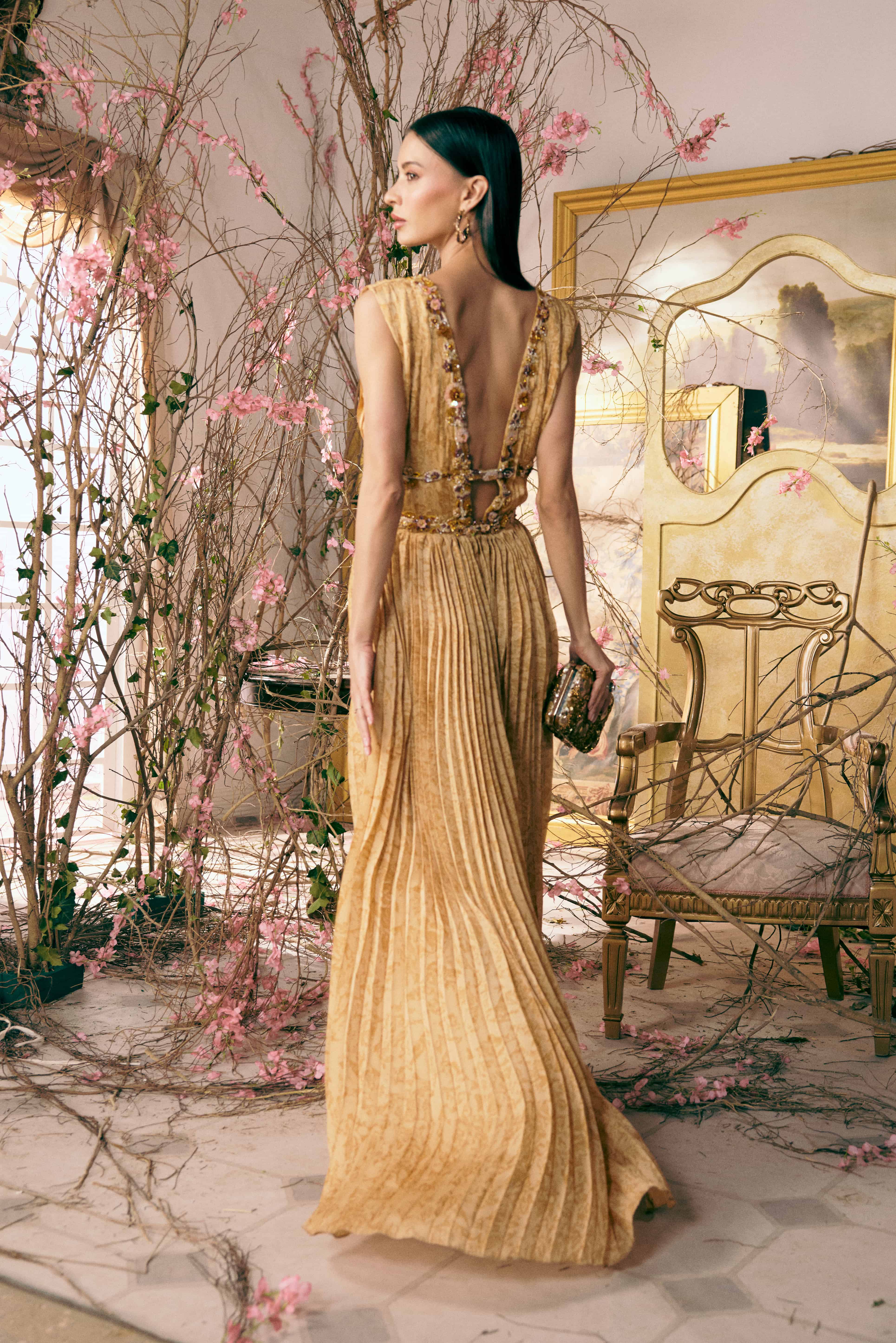 Woman in a gold dress standing in an elegant room with decorative elements.
