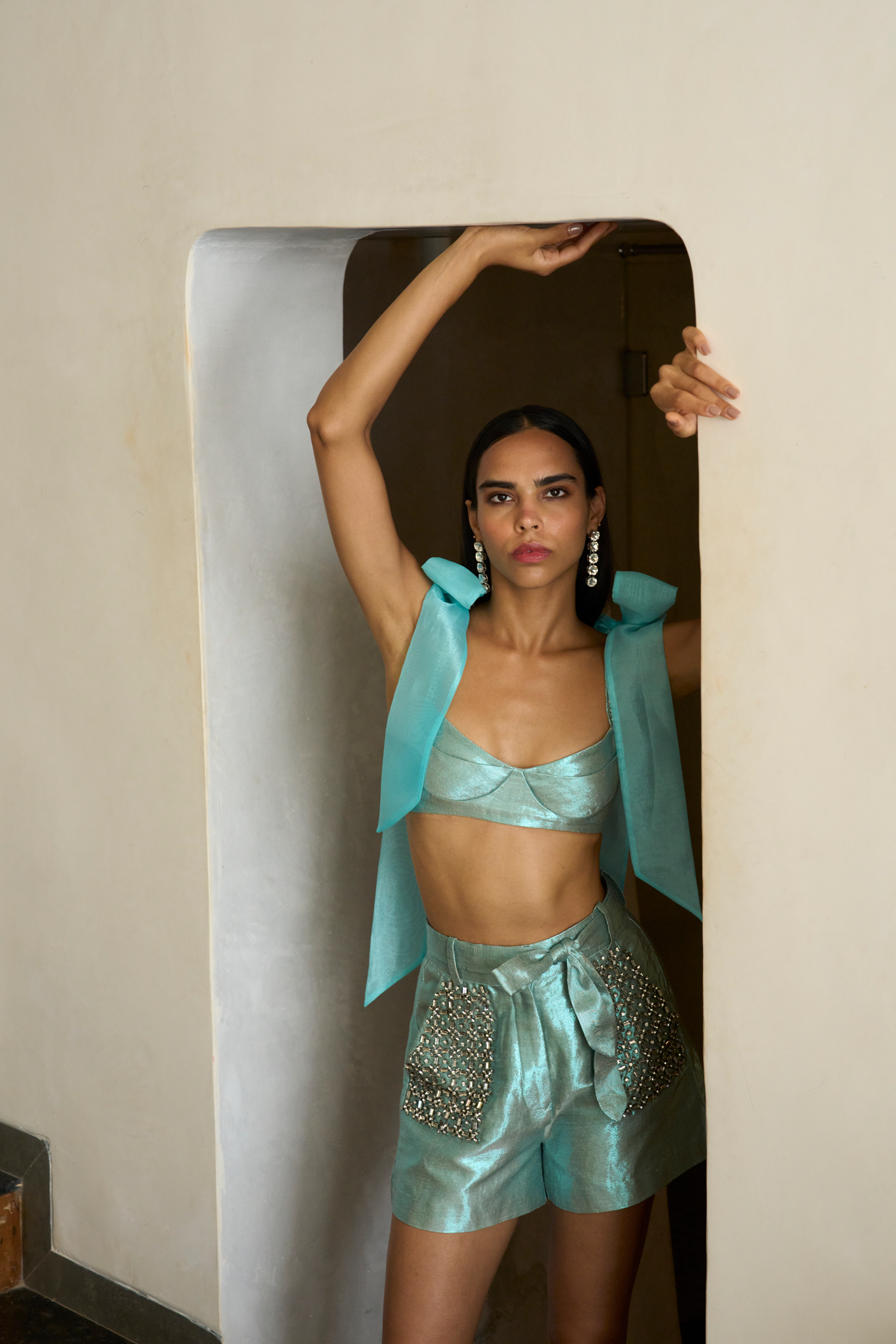 Woman in a teal outfit standing in front of a mirror.