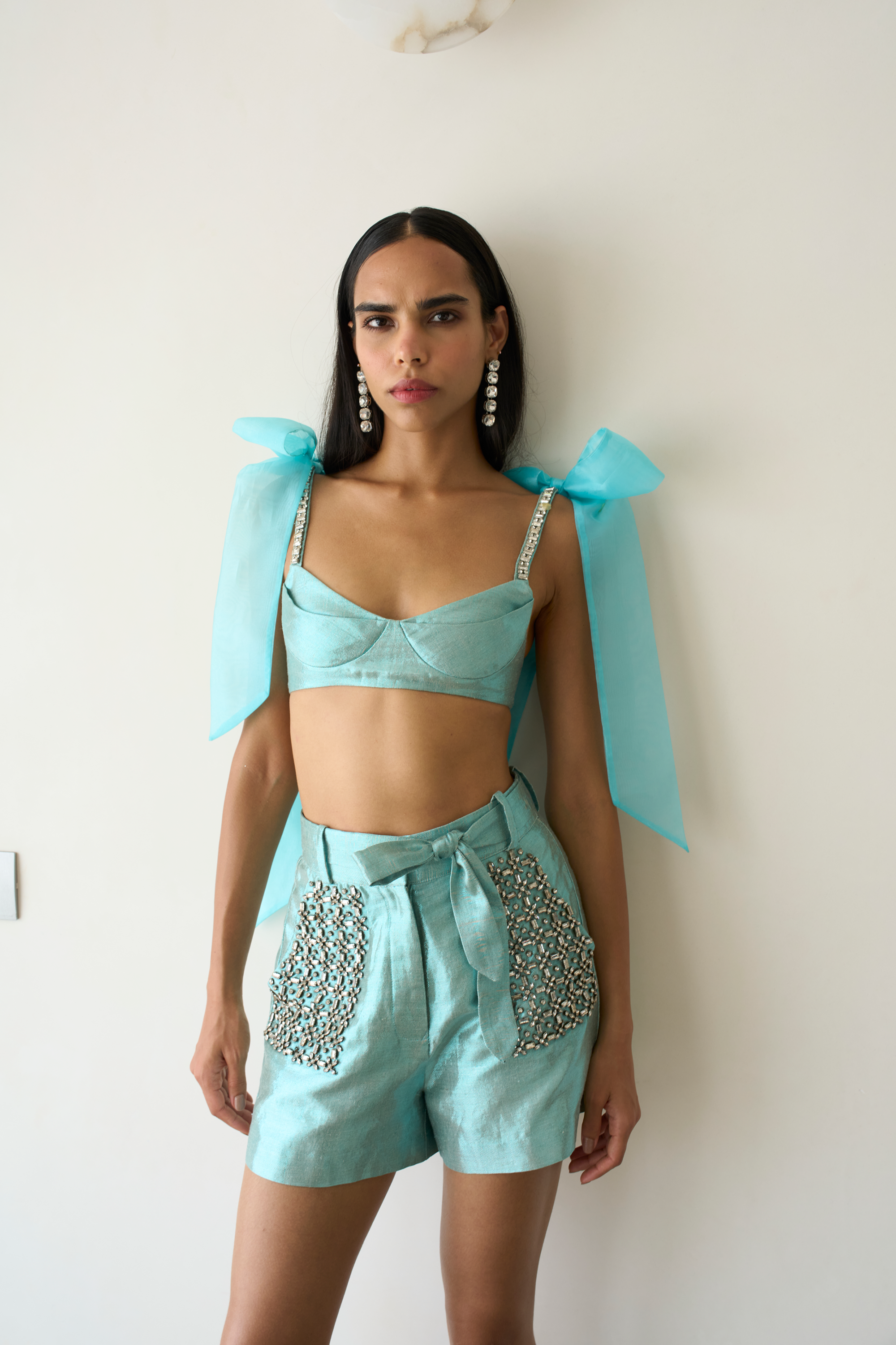 Woman wearing a light blue outfit with decorative elements against a white background
