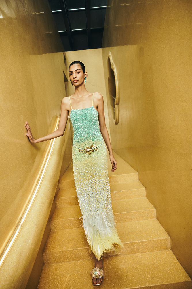 Woman in a gradient dress walking down a staircase in a gold-walled hallway