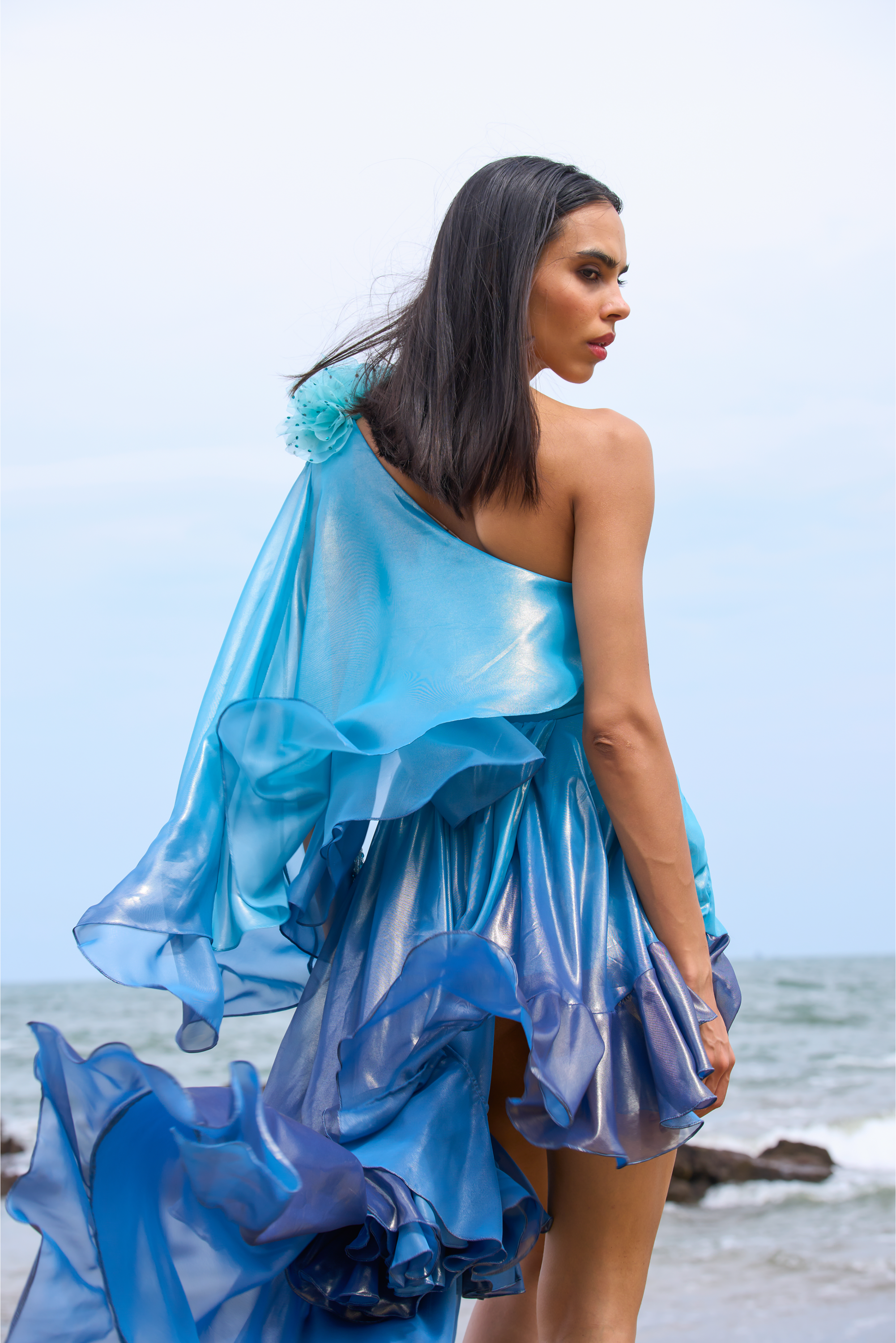 Woman in a blue dress standing on a beach with ocean view