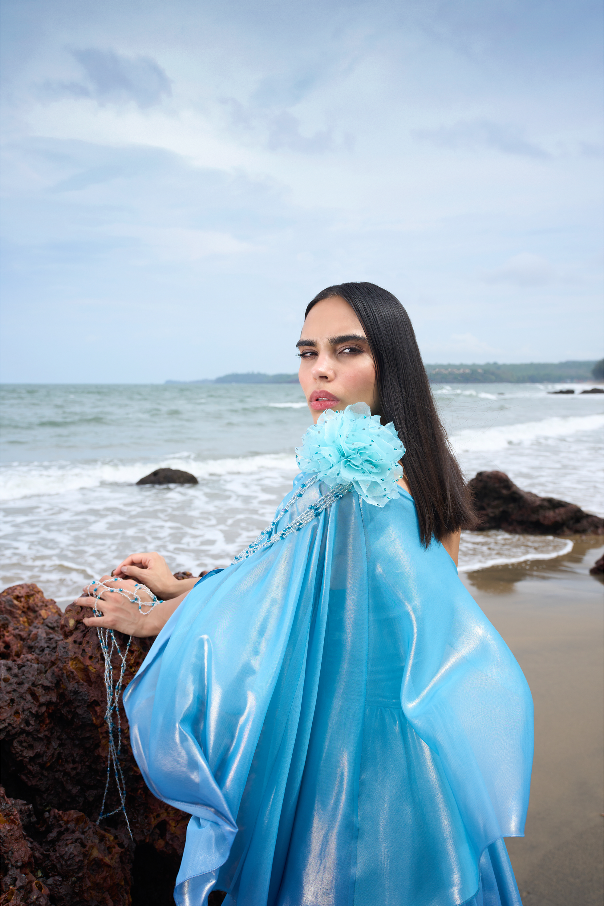 Woman in a blue dress sitting on a beach with ocean and sky in the background