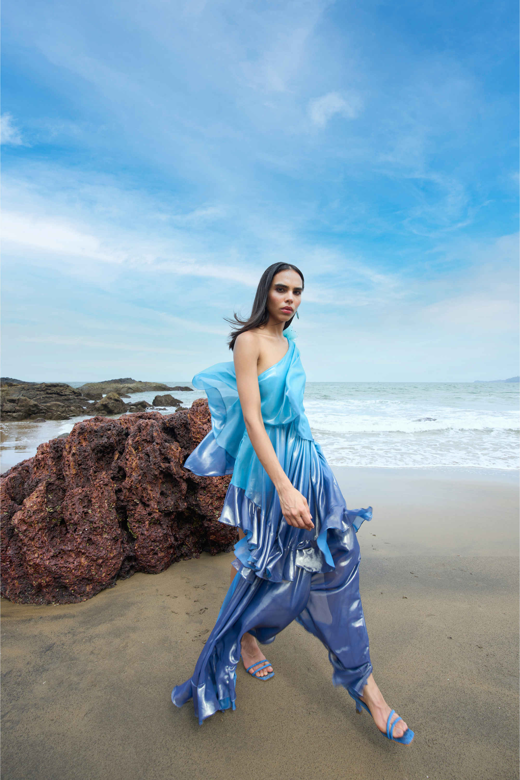Woman in a blue dress standing on a beach with ocean and sky in the background