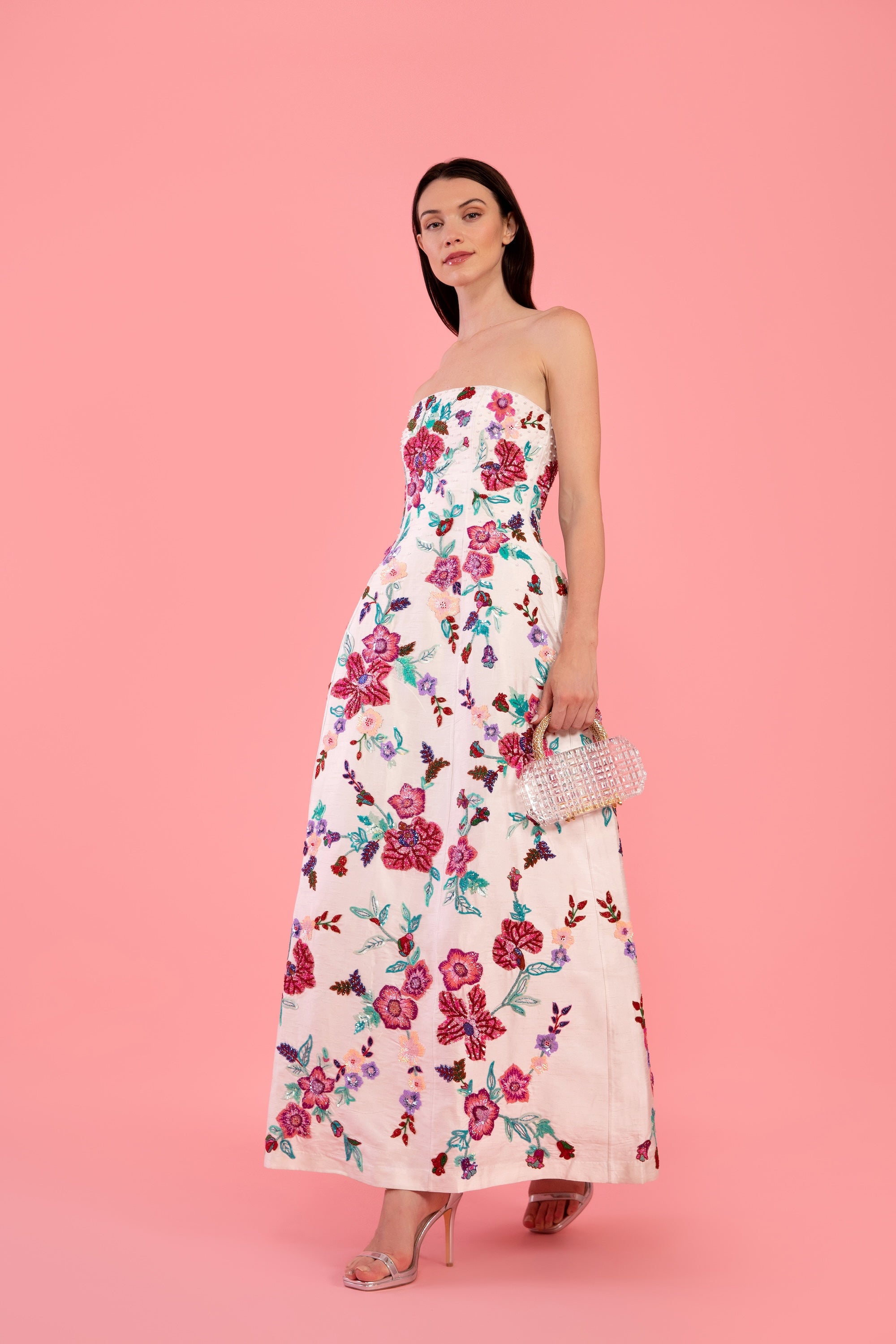 Woman wearing a white floral embroidered gown on a pink background
