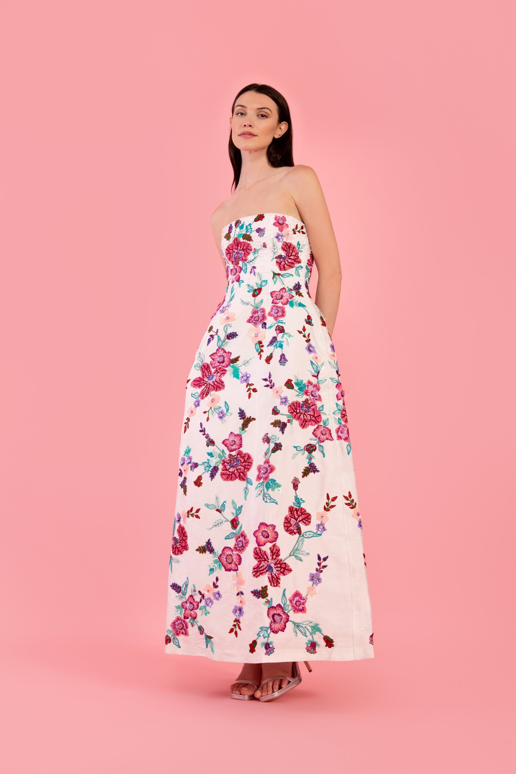 Woman wearing a strapless white floral embroidered gown on a pink background