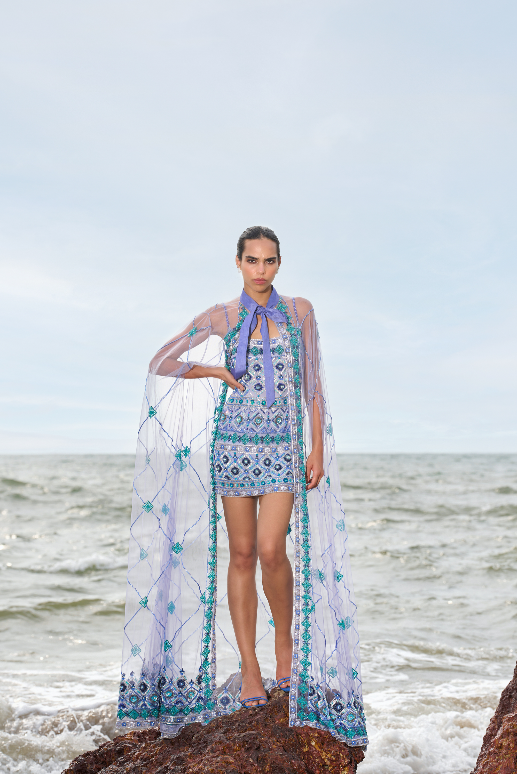 Woman in a patterned dress standing on a rock by the ocean
