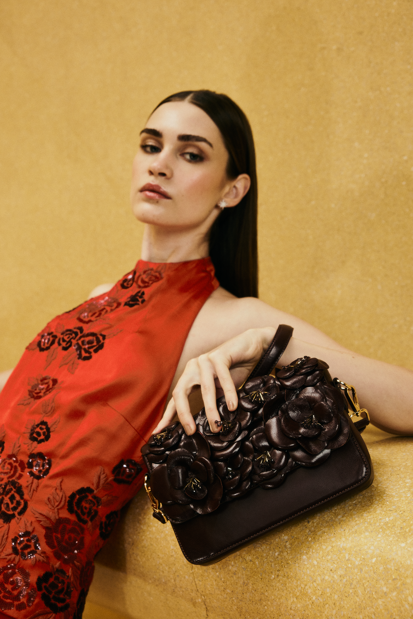 Woman holding a black handbag with floral details against a gold background