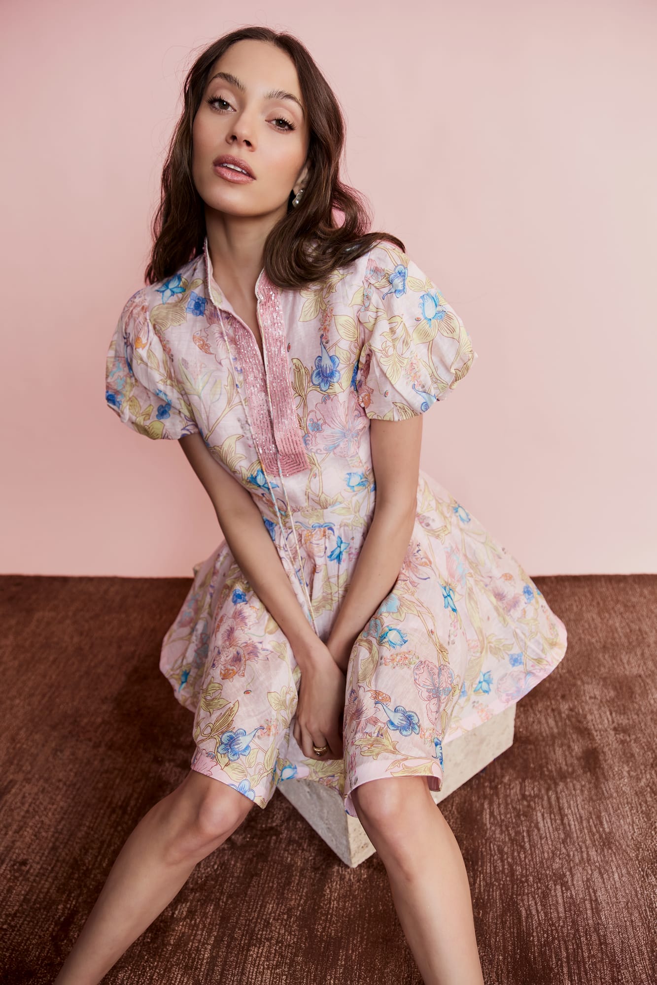 Woman wearing a floral dress sitting on a textured surface with a pink background