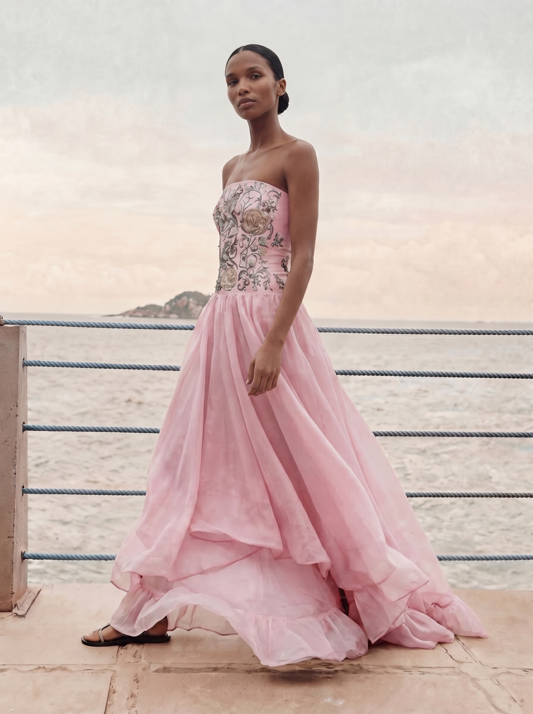 Woman in a pink strapless gown with floral embellishments standing on a wooden deck.