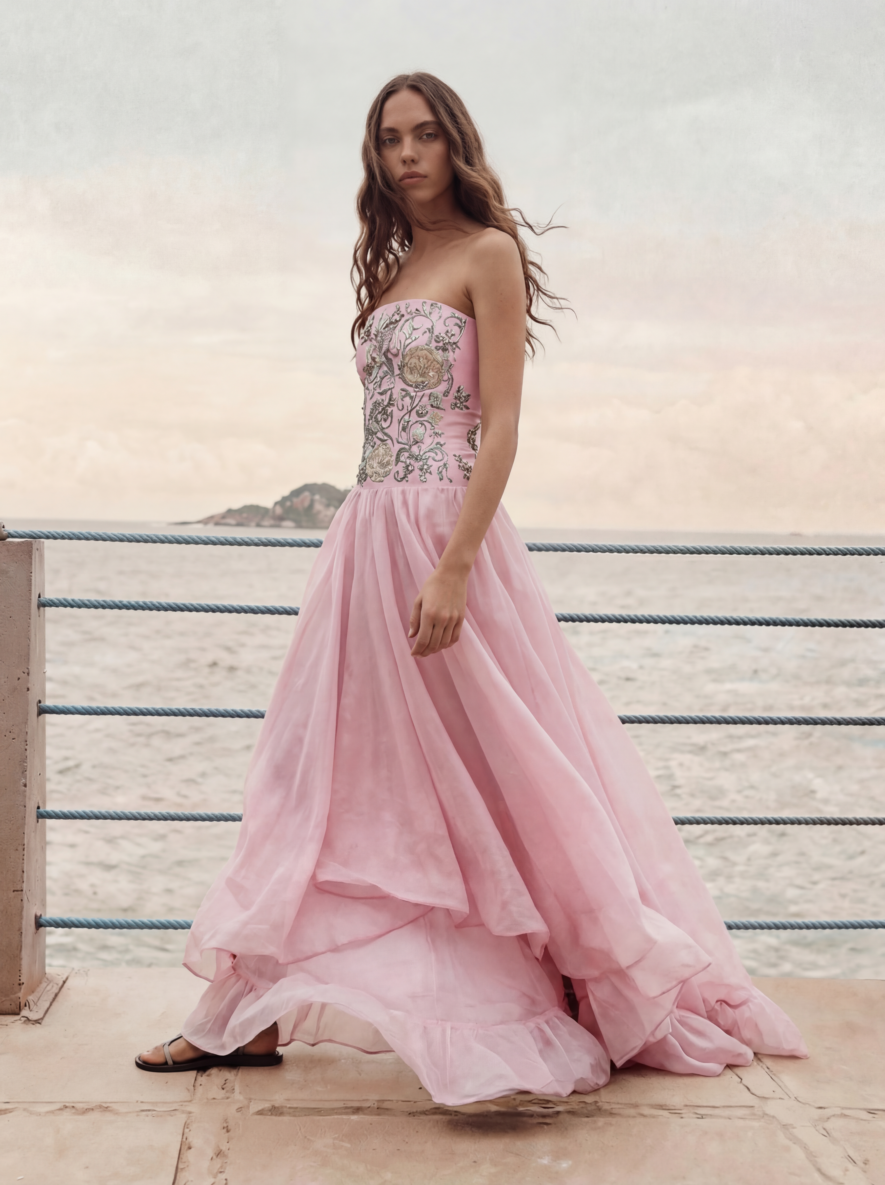 Woman in a pink strapless gown with floral details standing on a wooden deck.