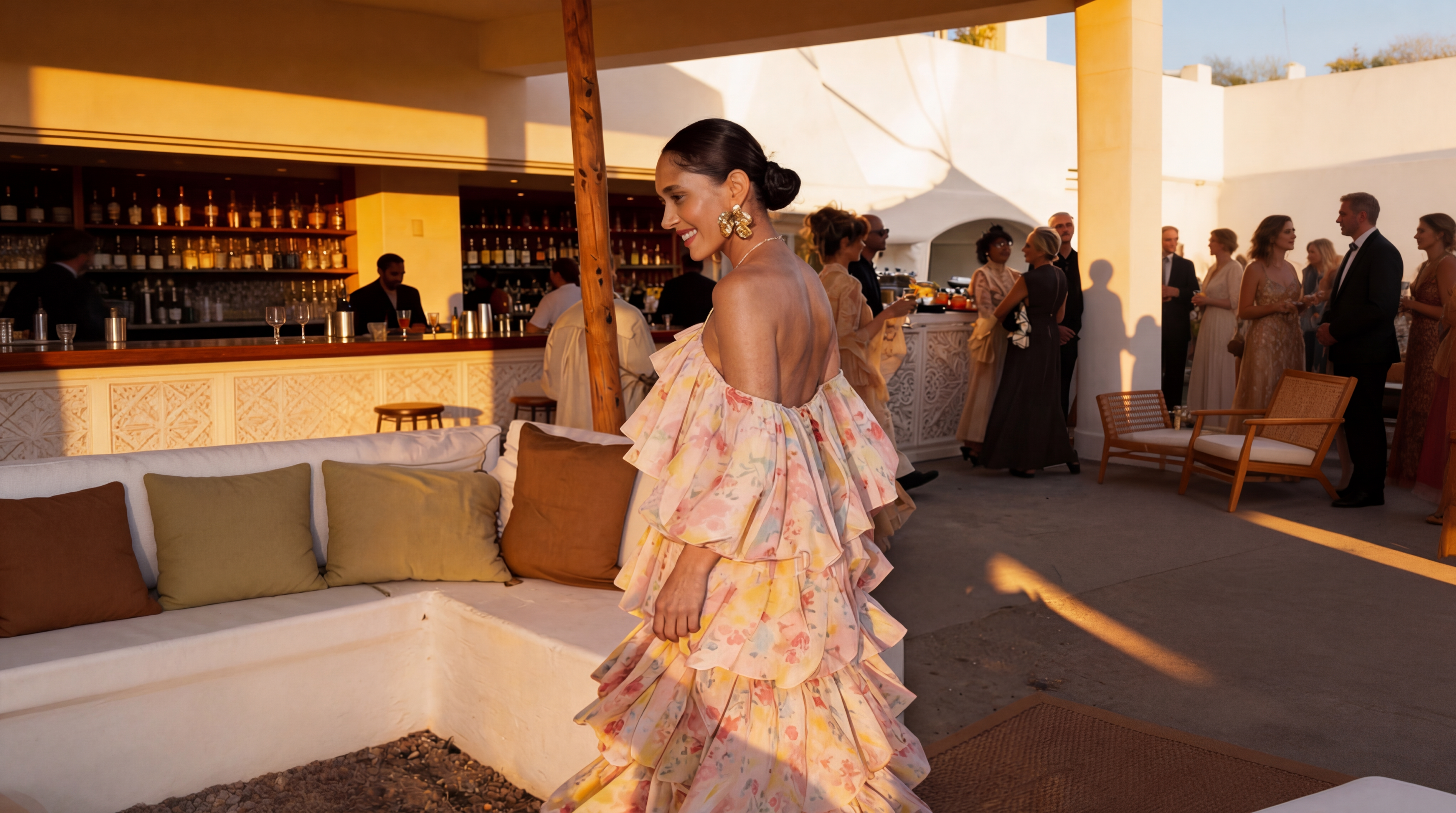 Woman in a floral dress standing in an outdoor setting with people and a bar in the background.