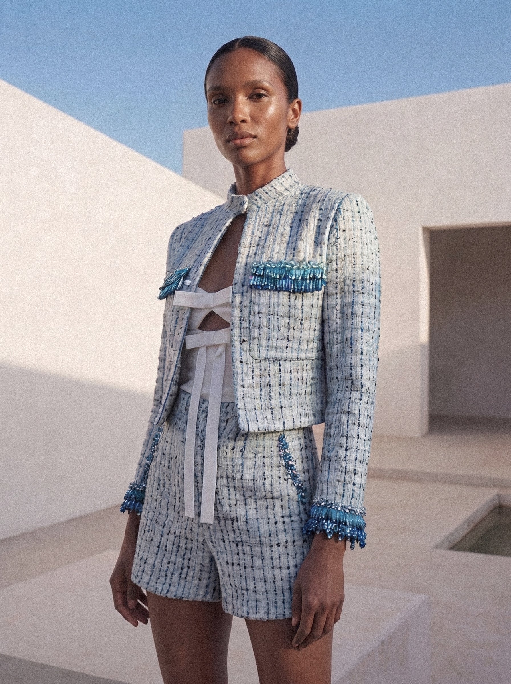 Woman wearing a blue and white checkered outfit with decorative elements in a sunlit outdoor setting.