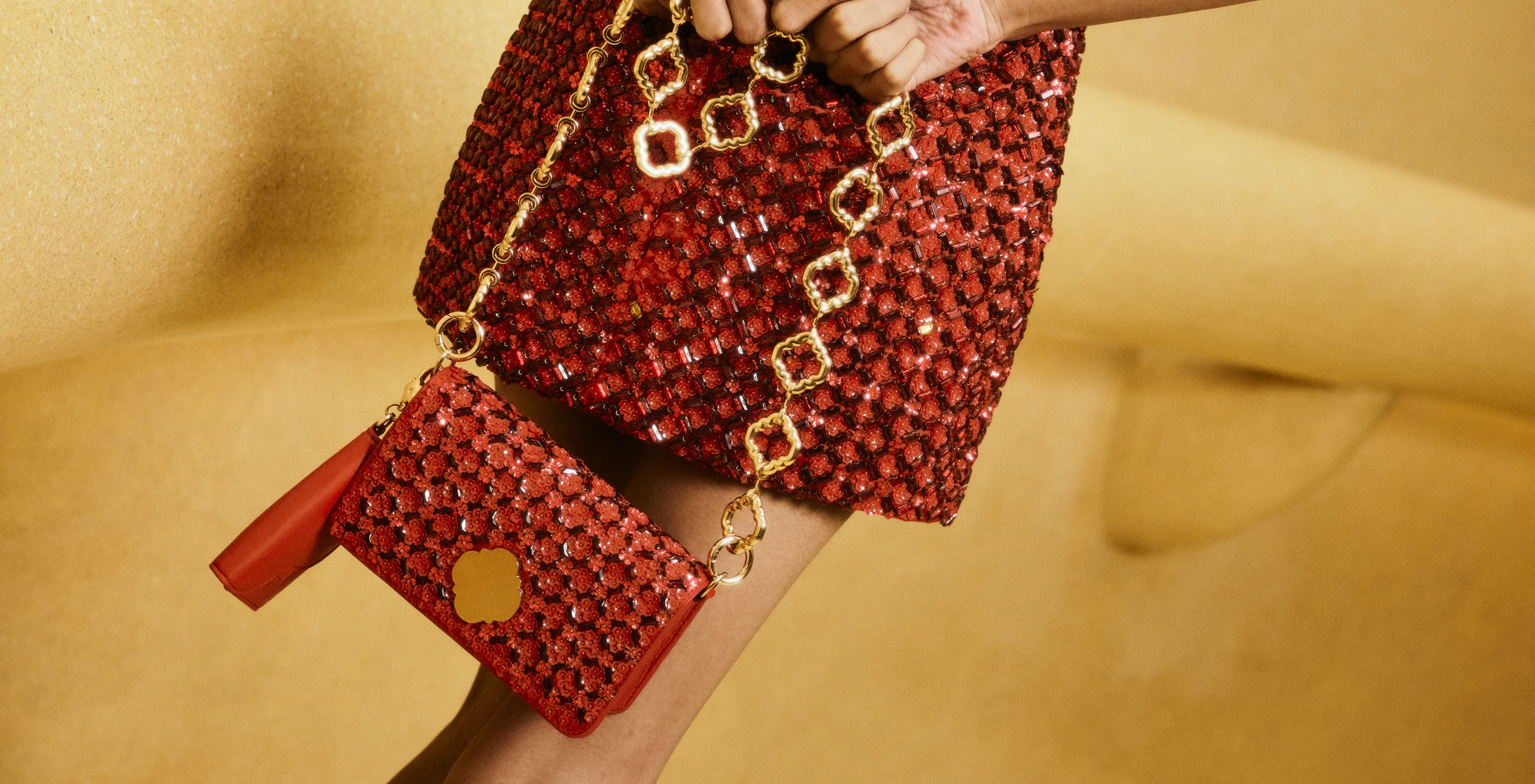 Red beaded handbag with gold chain strap held by a person on a beige background